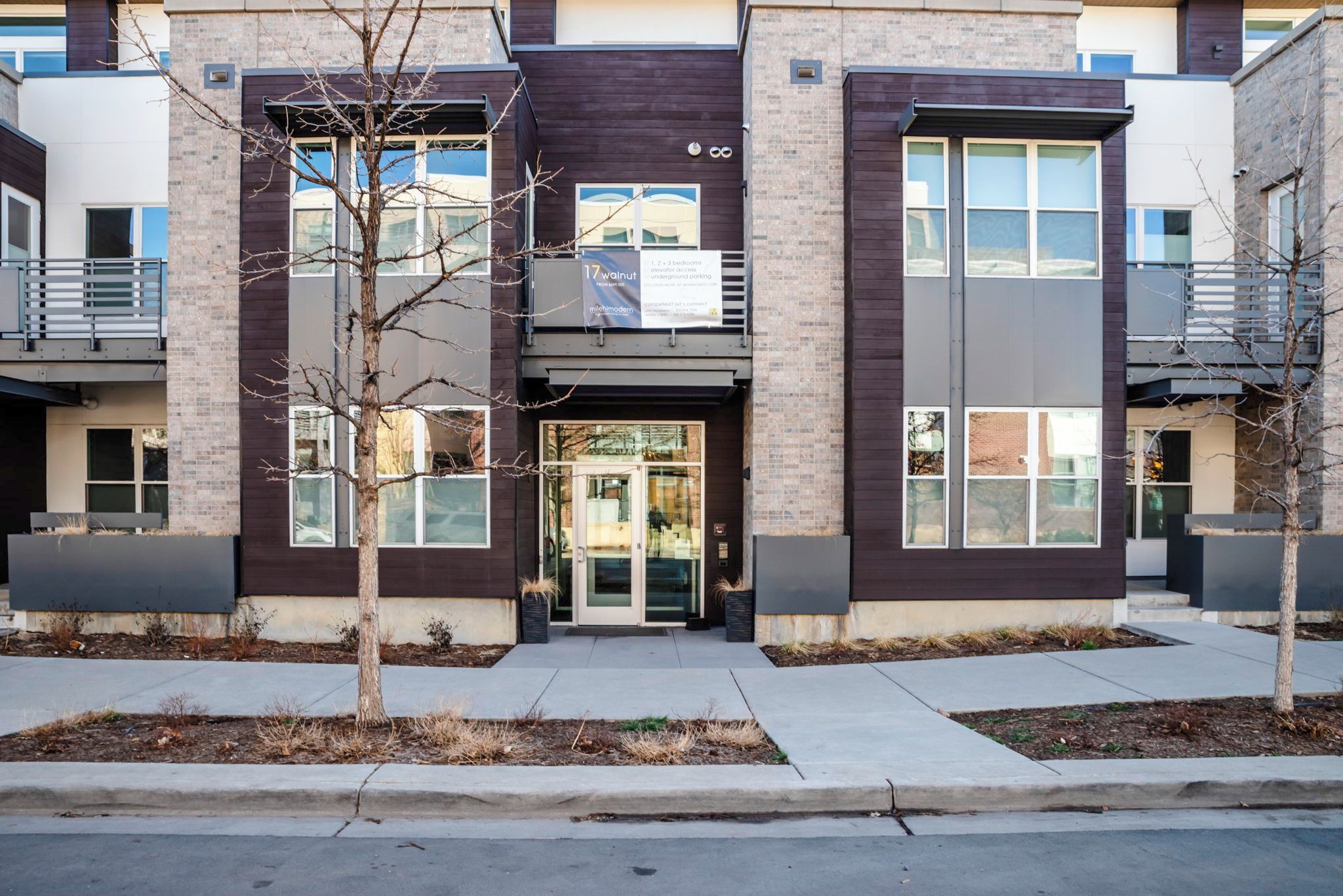 A modern apartment building with a central entrance, large windows, and a sign indicating 1, 2, and 3 bedroom units.
