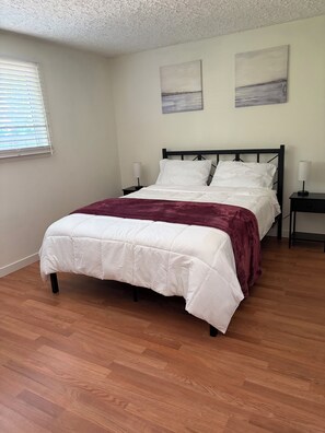 A bedroom with a bed, wooden flooring, and two wall-mounted paintings.