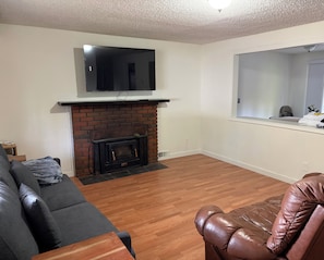 A living room with a fireplace, a flat-screen TV mounted above it, a brown leather armchair, a gray sofa, and a wooden coffee table.