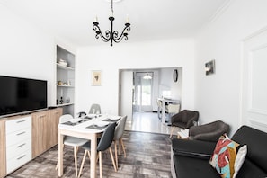 A modern kitchen with a flat-screen TV, dining table set for four, and a sofa with a colorful pillow. - Les Vignettes - LOISY EN BRIE (LOISY EN BRIE)