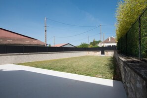 A fenced backyard with a grassy area and a concrete patio. - Les Vignettes - LOISY EN BRIE (LOISY EN BRIE)