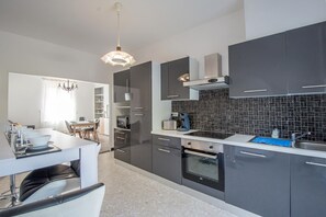 A modern kitchen with dark cabinets, a black tiled backsplash, and a dining area with a white table and chairs. - Les Vignettes - LOISY EN BRIE (LOISY EN BRIE)