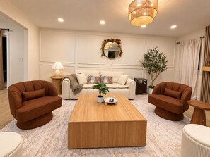 Un salon comprenant un canapé, une table basse, deux fauteuils, une lampe, un miroir et une plante.