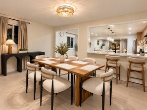 A modern dining area with a wooden table and chairs, a console table with a lamp, and a view into the kitchen. - Luxury Remodel Disney Retreat With Game Room & Private Yard (Anaheim)