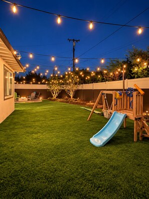 A backyard with a wooden play structure, a blue slide, and string lights. - Luxury Remodel Disney Retreat With Game Room & Private Yard (Anaheim)