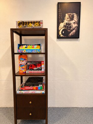 A bookshelf with various board games and a framed picture on the wall. - Luxury Remodel Disney Retreat With Game Room & Private Yard (Anaheim)