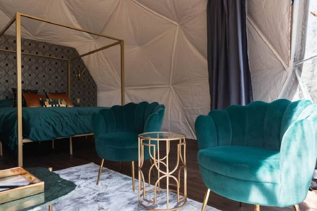 A tented room with a four-poster bed, teal upholstered chairs, and a marble-patterned rug.