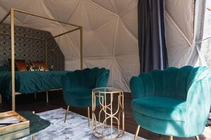 A tented room with a four-poster bed, teal upholstered chairs, and a marble-patterned rug.