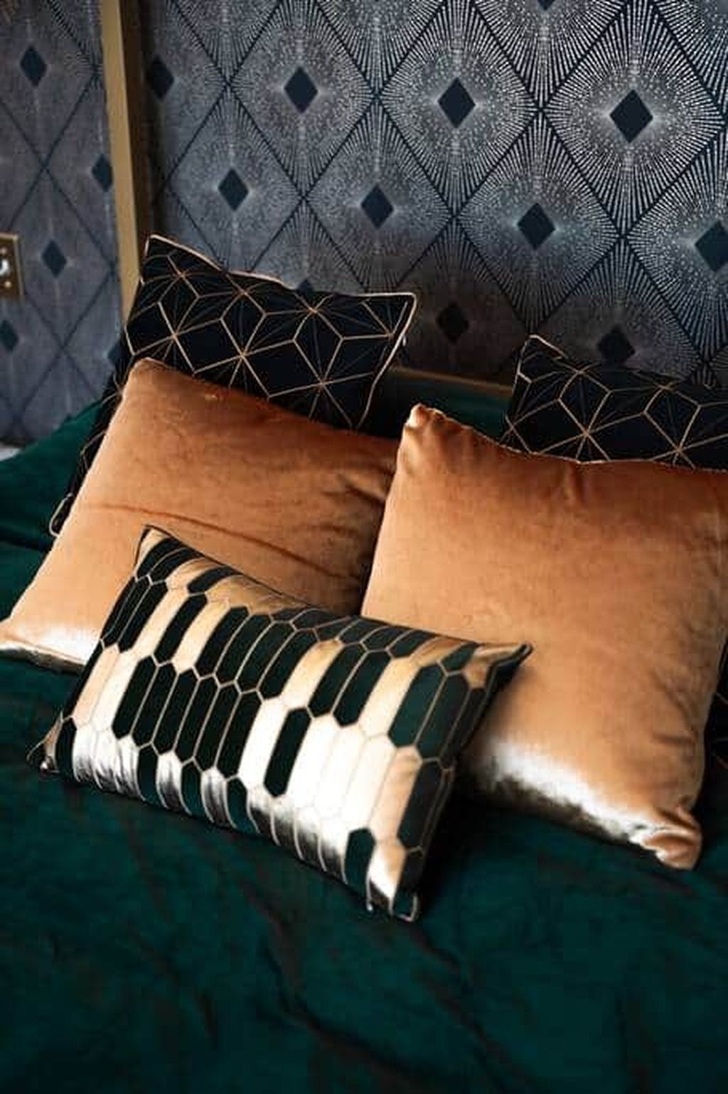 A bed with a green bedspread and three pillows with geometric patterns.