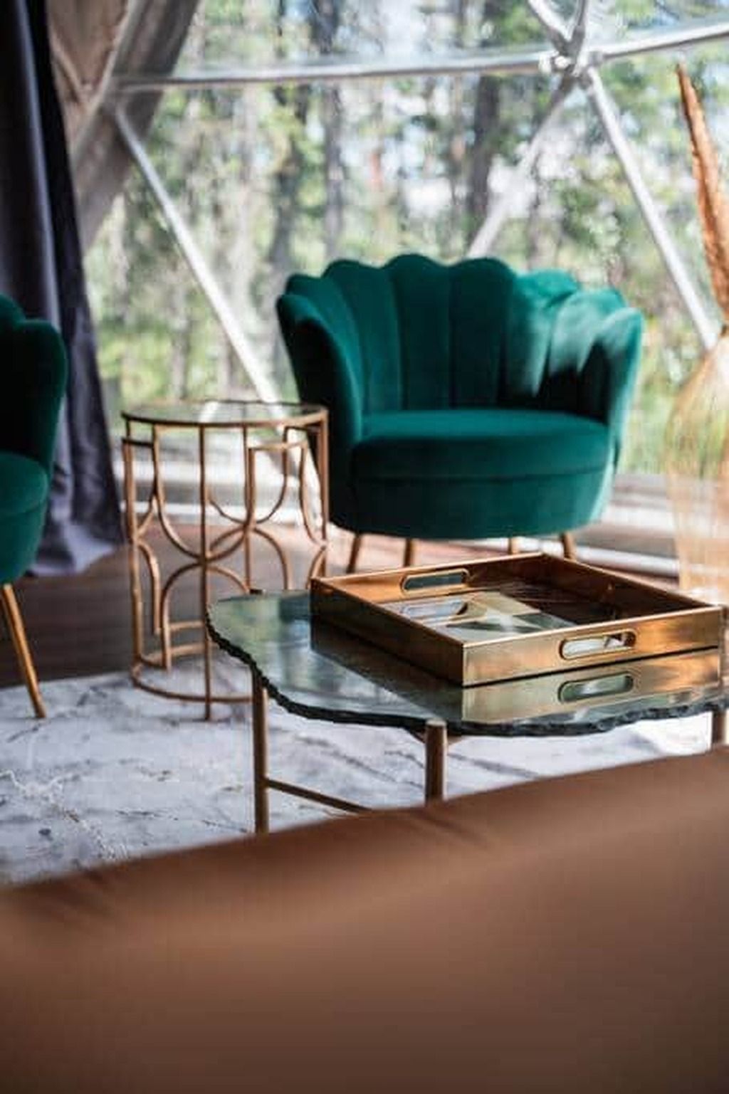 A tent interior with a green upholstered chair, a glass-top table with a tray, and a gold-framed side table.