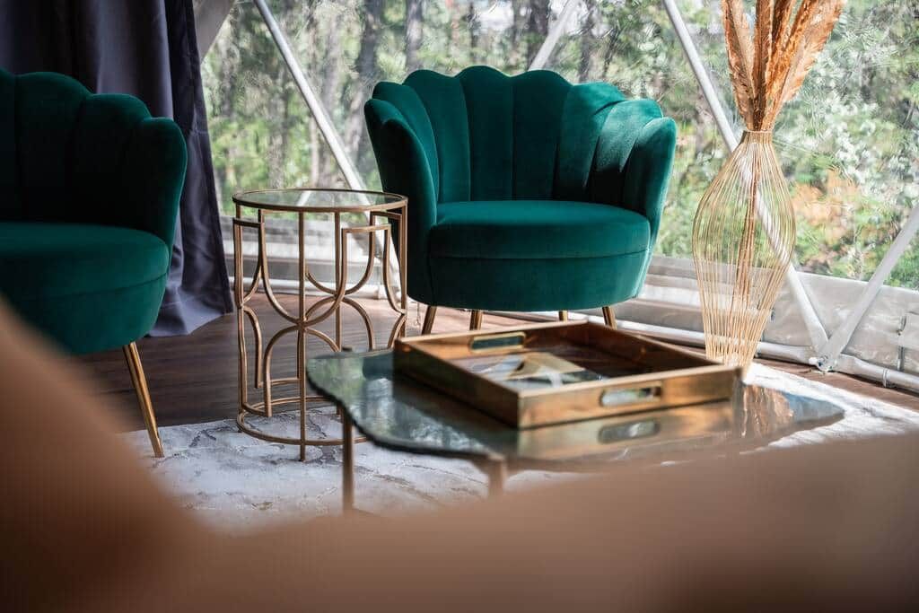 Une pièce avec deux fauteuils verts, une petite table ronde et un vase contenant des plantes séchées.