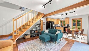 A spacious living area with a wooden staircase, a teal sofa, and a kitchen with wooden cabinets. - Cozy 2-bedroom chalet in delightful Gunstock Acres (Gilford)