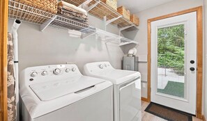 A laundry area with two white front-loading washers and dryers, a white ceiling vent, and a door leading to a green outdoor area. - Cozy 2-bedroom chalet in delightful Gunstock Acres (Gilford)