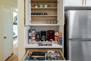 Een keuken met een roestvrijstalen koelkast, een koffiezetapparaat en diverse mokken en bekers op planken.