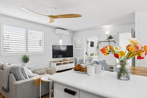 Een moderne keuken met witte bakstenen muren, een houten plafondventilator, een flatscreen televisie en een eethoek met een witte tafel en stoelen.
