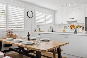 Une cuisine moderne avec des meubles blancs, une table à manger en bois pour quatre personnes et une horloge au mur.