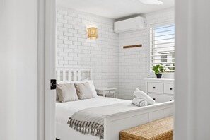 Een slaapkamer met witte bakstenen wanden, een bed, nachtkastje en een raam met zonwering.