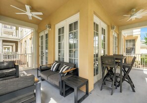 A covered outdoor seating area with a sofa and a table, large windows, and ceiling fans. - Kissimmee Family Home | 3BR, 2BA & Laundry (Kissimee)