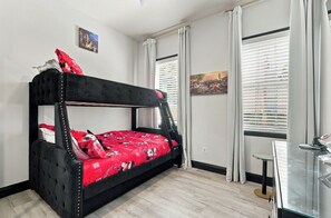 A bunk bed with a red Mickey Mouse themed bedspread, a small table with a telephone, and a window with blinds. - Kissimmee Family Home | 3BR, 2BA & Laundry (Kissimee)