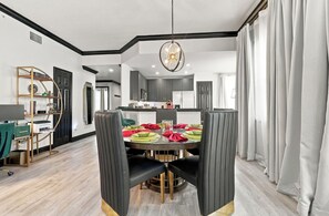 Een eetgedeelte met een ronde tafel, zwarte stoelen met bekleding en een kroonluchter.