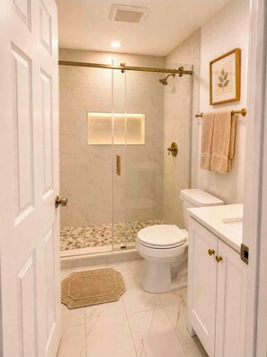 A bathroom with a glass-enclosed shower, a toilet, and a vanity with a towel hanging on the wall. - Modern Austin Retreat Near Airport & Downtown (Austin)