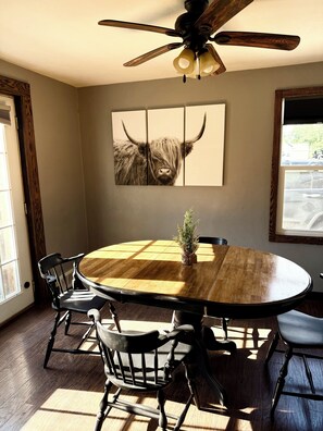 A dining area with a round wooden table, black chairs, and a ceiling fan. - Boho Bungalow walking distance from Notre Dame (South Bend)