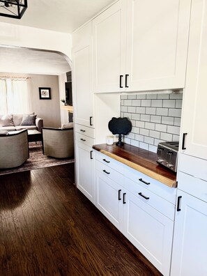 A modern kitchen with white cabinetry, a wooden countertop, and a tiled backsplash. - Boho Bungalow walking distance from Notre Dame (South Bend)