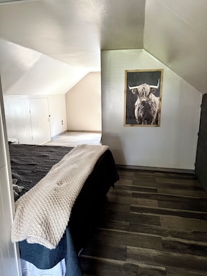 A bedroom with a bed, a wooden floor, a painting of a bull, and a sloped ceiling. - Boho Bungalow walking distance from Notre Dame (South Bend)