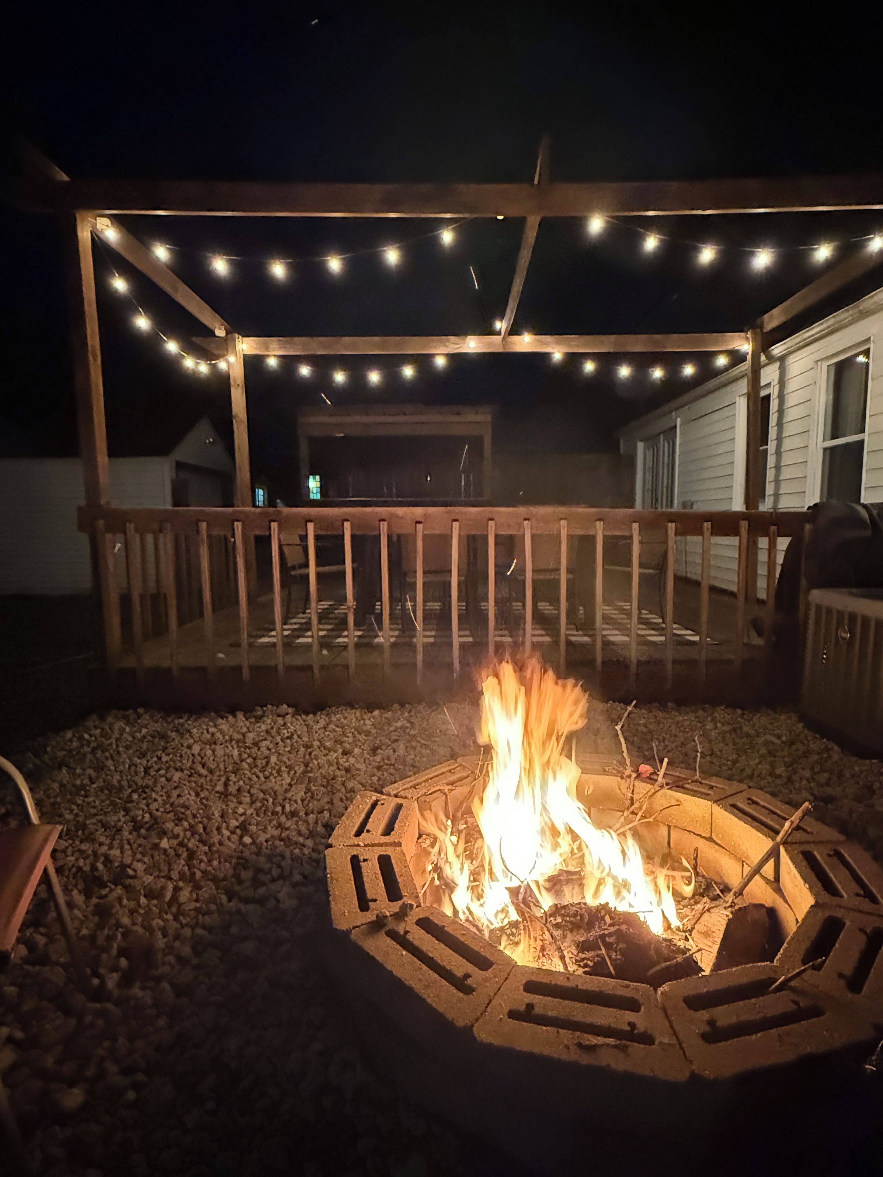 A fire pit with a wooden deck and string lights.