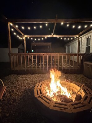 A fire pit with a wooden deck and string lights. - Boho Bungalow walking distance from Notre Dame (South Bend)