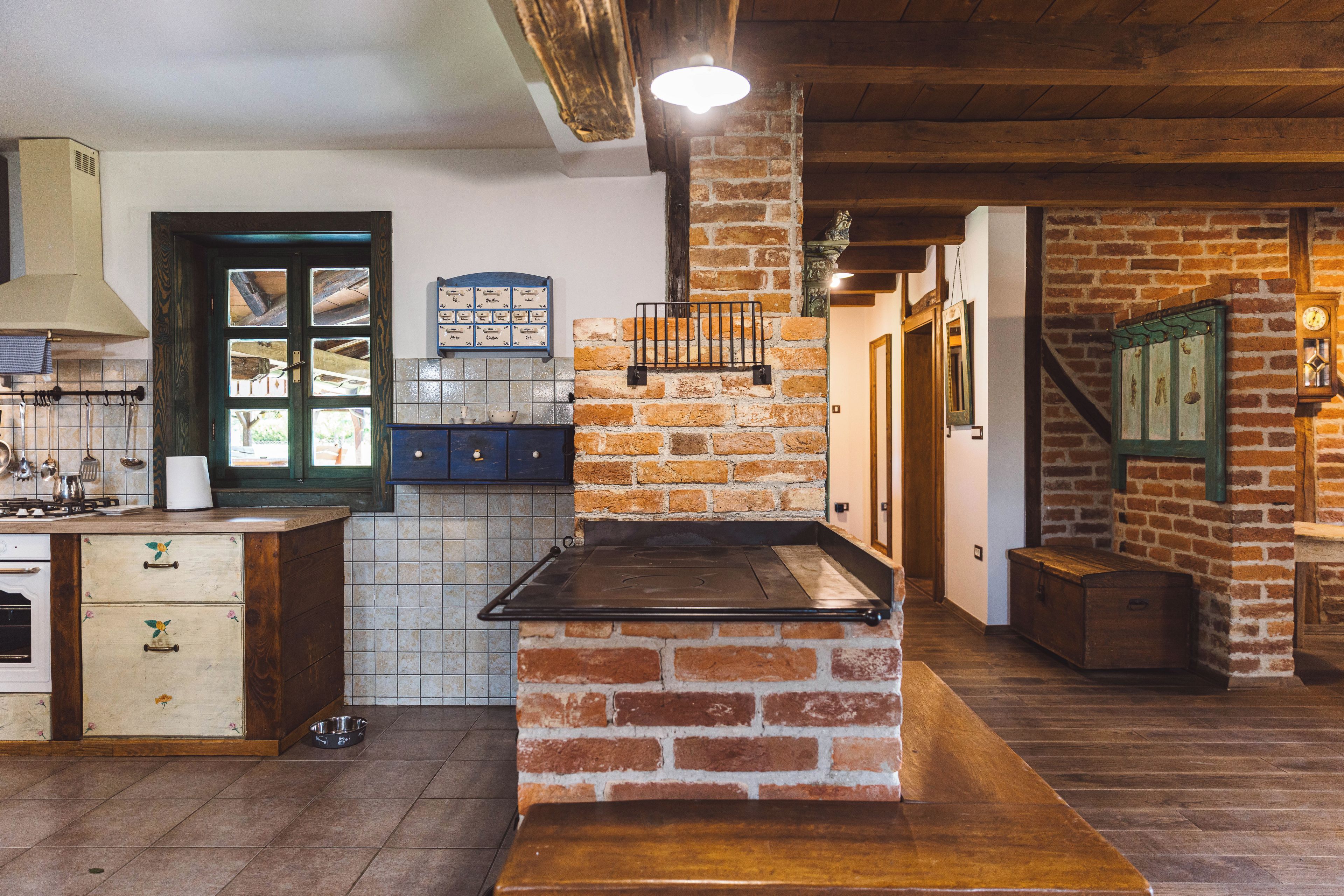 A rustic kitchen with a brick oven, wooden cabinets, and a tiled backsplash.