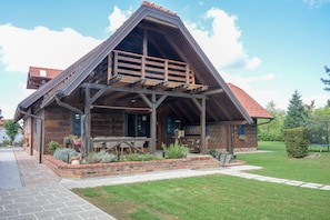 A wooden cabin with a sloped roof, a balcony, and a patio area with outdoor seating. - Charming Wooden Holiday Home in Zagorje with Jacuzzi, Sauna and Large Estate (Donja Stubica)
