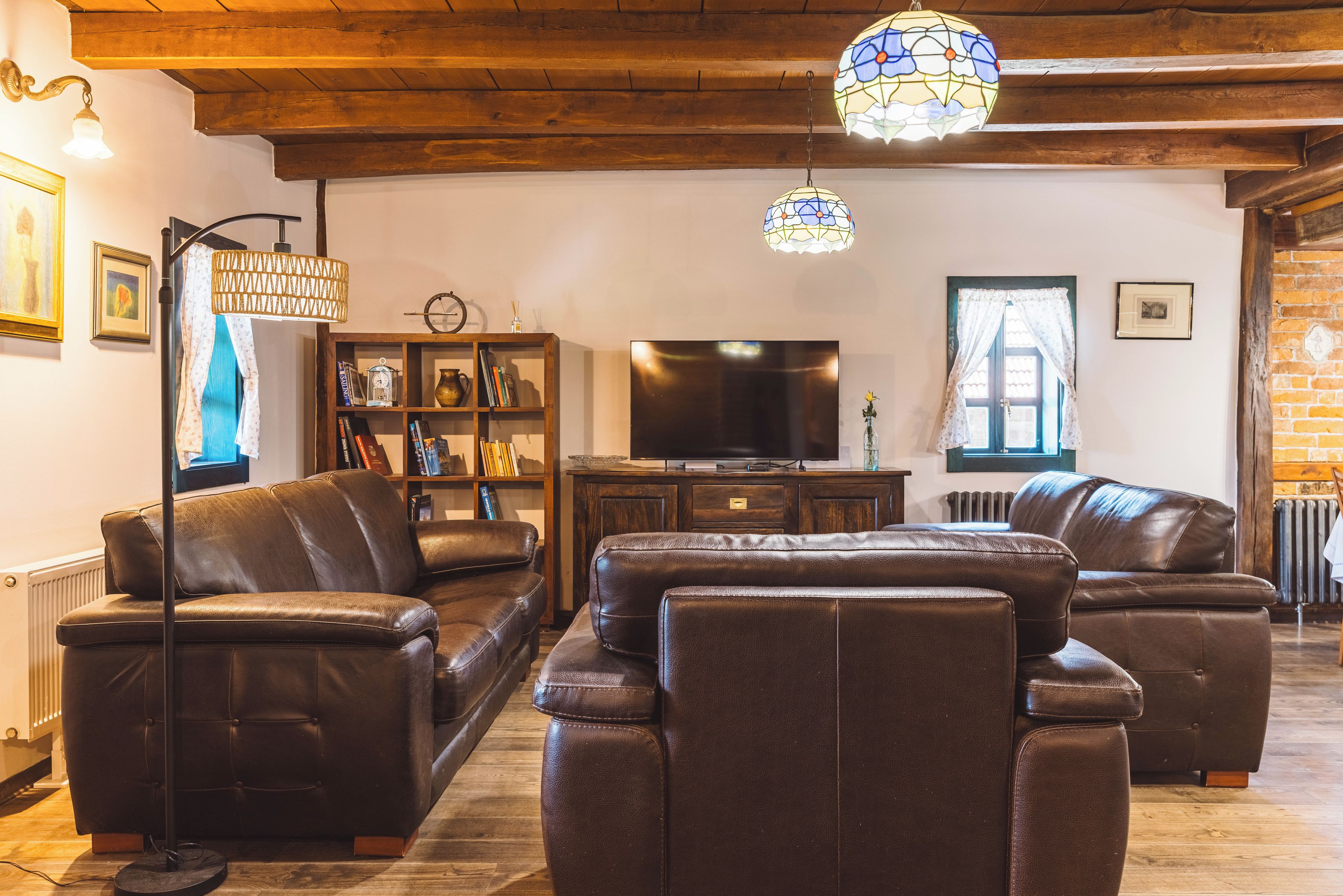 Ein Wohnzimmer mit Ledersofas, einem Fernseher, einem Bücherregal und einer dekorativen Lampe.