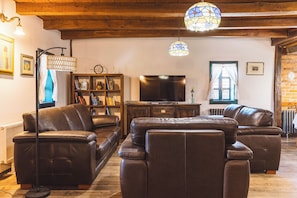 A living room with leather sofas, a television, a bookshelf, and a decorative lamp. - Charming Wooden Holiday Home in Zagorje with Jacuzzi, Sauna and Large Estate (Donja Stubica)