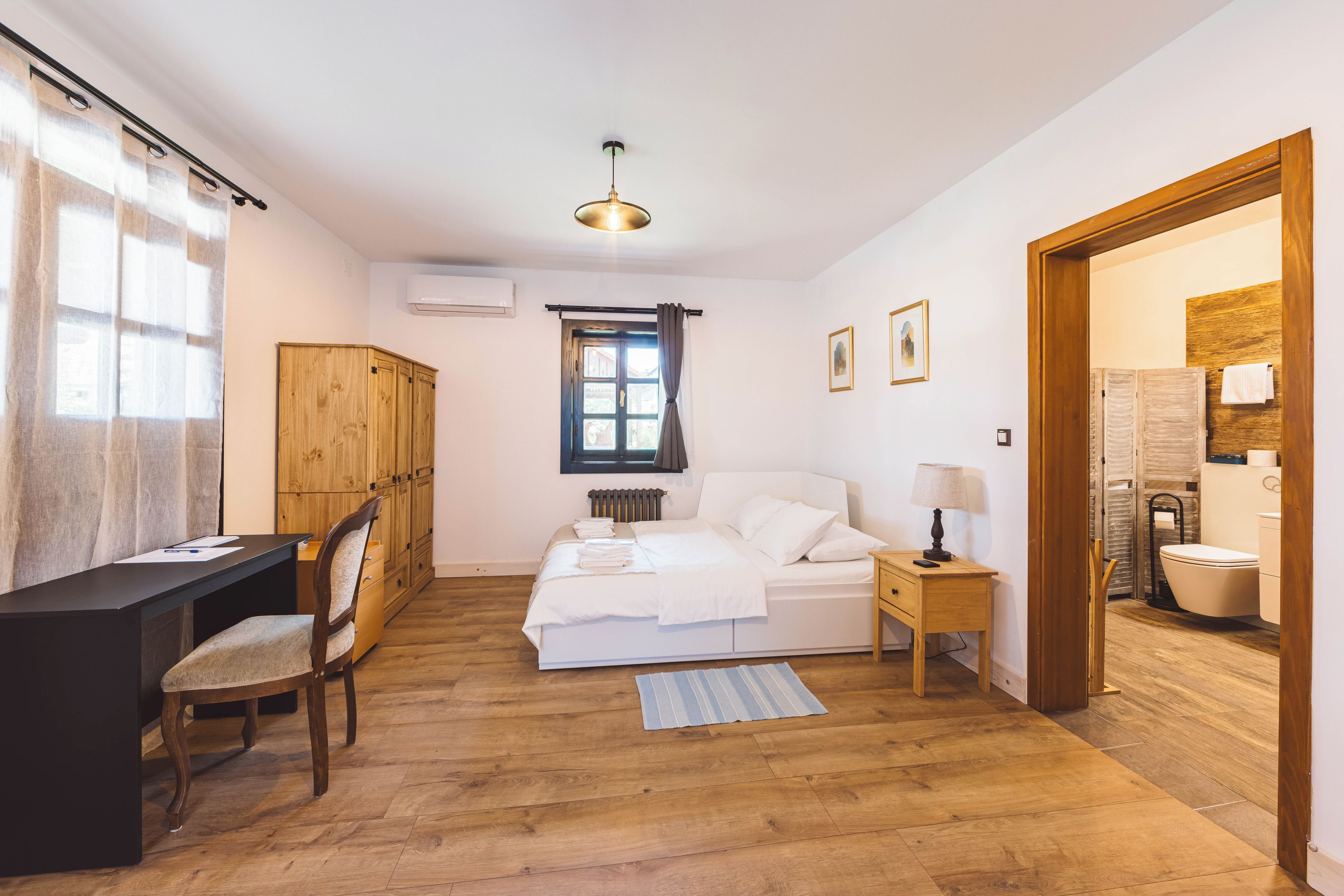 A bedroom with a bed, bedside table, chair, desk, and a window with curtains.