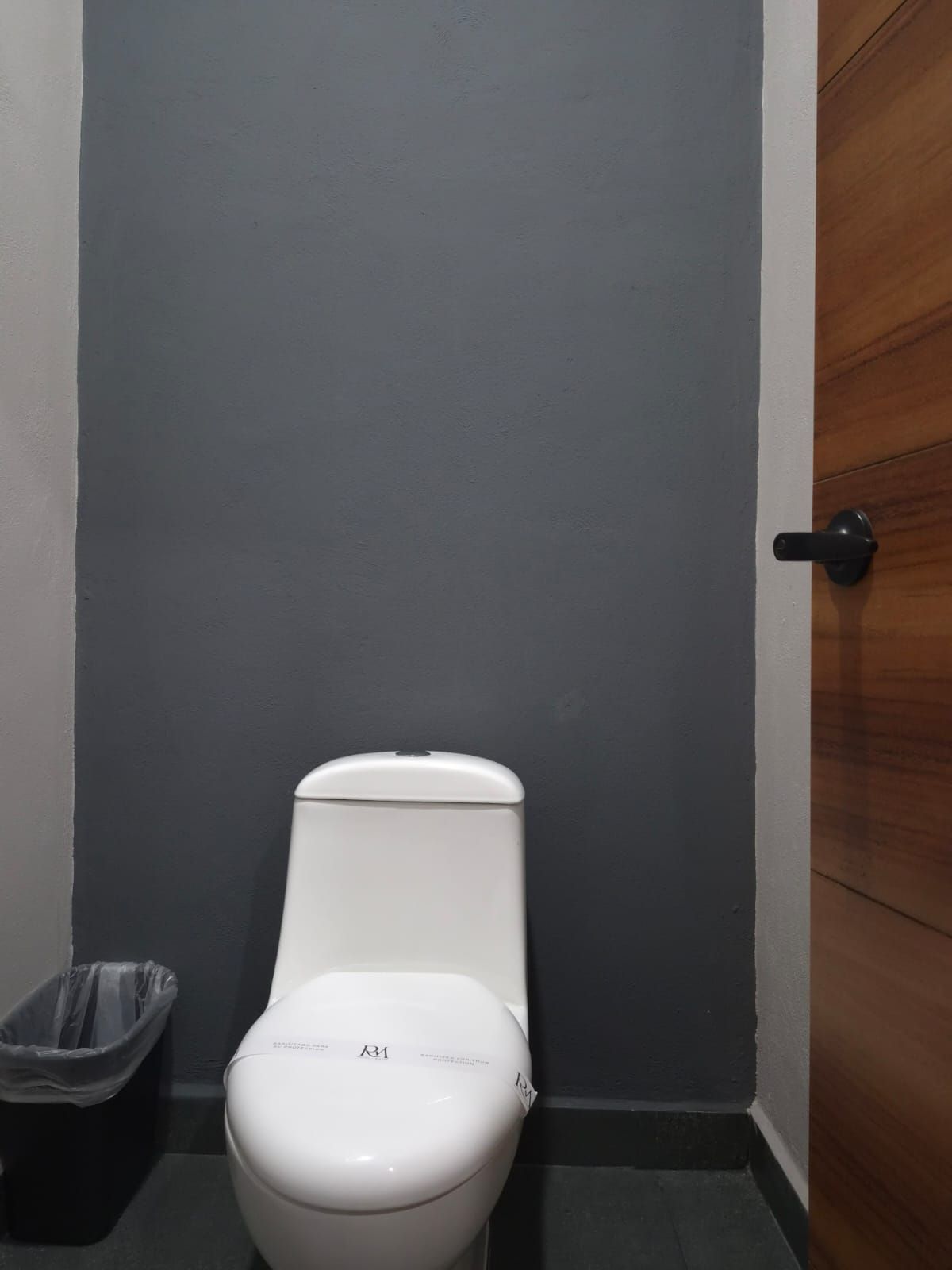Un inodoro blanco en una esquina, con una pared negra y una puerta de madera.