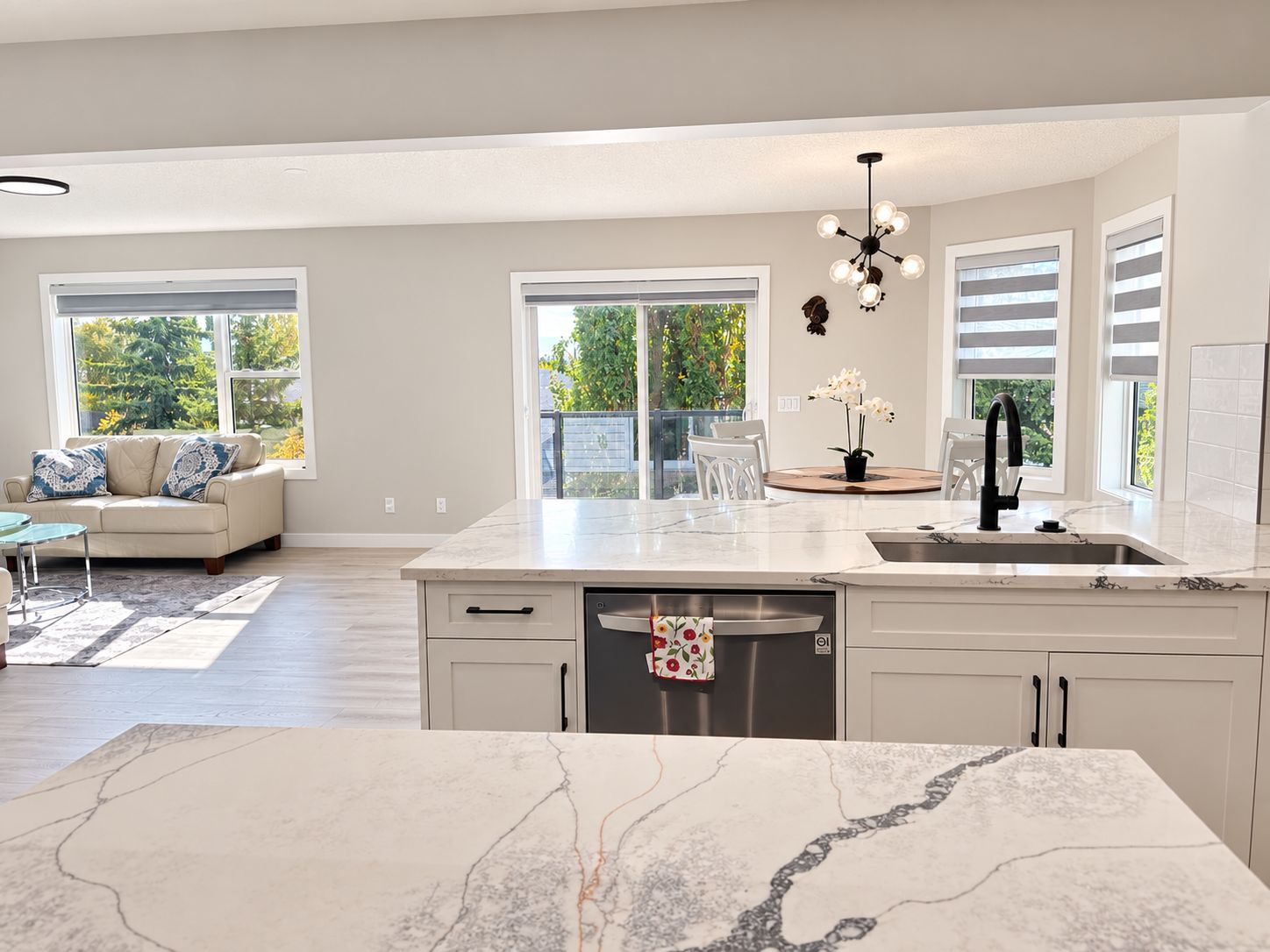 A modern kitchen with a marble countertop, a dishwasher, and a dining area with a sofa and chairs.