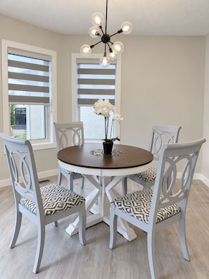 A dining area with a round table, six chairs, a chandelier, and a window with blinds. - Panorama Hills Manor | Private Luxury Main & Upper | Near YYC, Easy Banff Access (Calgary)