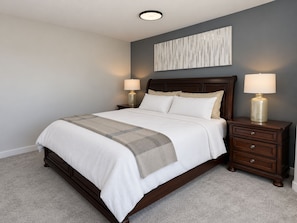 A bedroom with a large bed, two bedside tables with lamps, a headboard, and a wall-mounted artwork. - Panorama Hills Manor | Private Luxury Main & Upper | Near YYC, Easy Banff Access (Calgary)