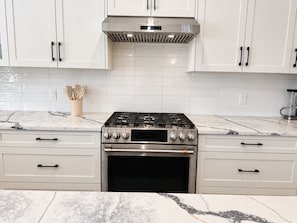 A kitchen with white cabinets, a stainless steel stove, and a marble countertop. - Panorama Hills Manor | Private Luxury Main & Upper | Near YYC, Easy Banff Access (Calgary)