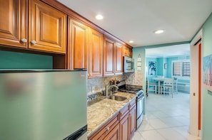 A kitchen with wooden cabinets, a stainless steel refrigerator, a granite countertop, and a dining area with a table and chairs. - Stay at Bluewater with Balcony,Beach & Pool Access (Myrtle Beach)