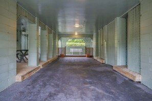 Un espacio al aire libre techado con piso de concreto, bancos de madera y vista a follaje a través de una estructura de celosía.