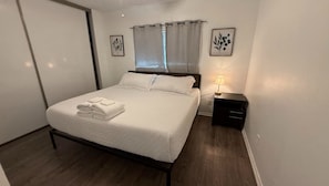 A neatly made bed with folded towels, a bedside table with a lamp, and a window with curtains. - Cozy Viva Sanriveria Rental 3Bed2.5 Bath hosts 8 people- near Seaworld,1604 W Lp (San Antonio)