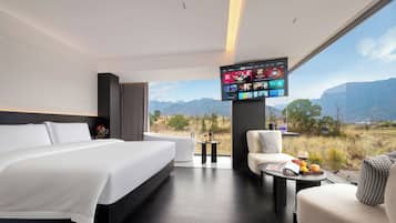 A modern hotel room with a large bed, a seating area with a view, and a flat-screen TV mounted on the wall.