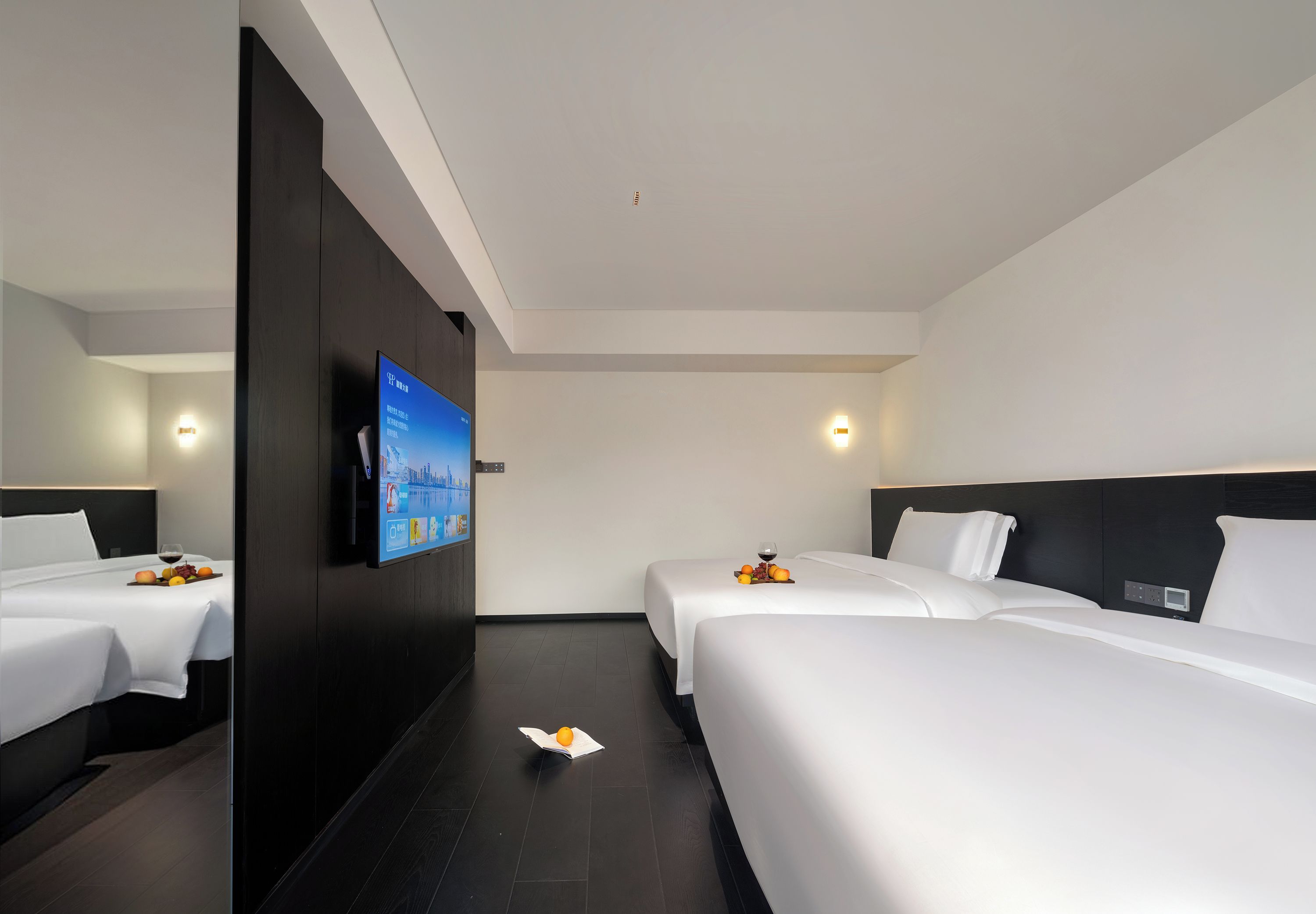 Een hotelkamer met twee bedden, een flatscreen televisie aan de muur en een kleine tafel met fruit en een glas wijn.