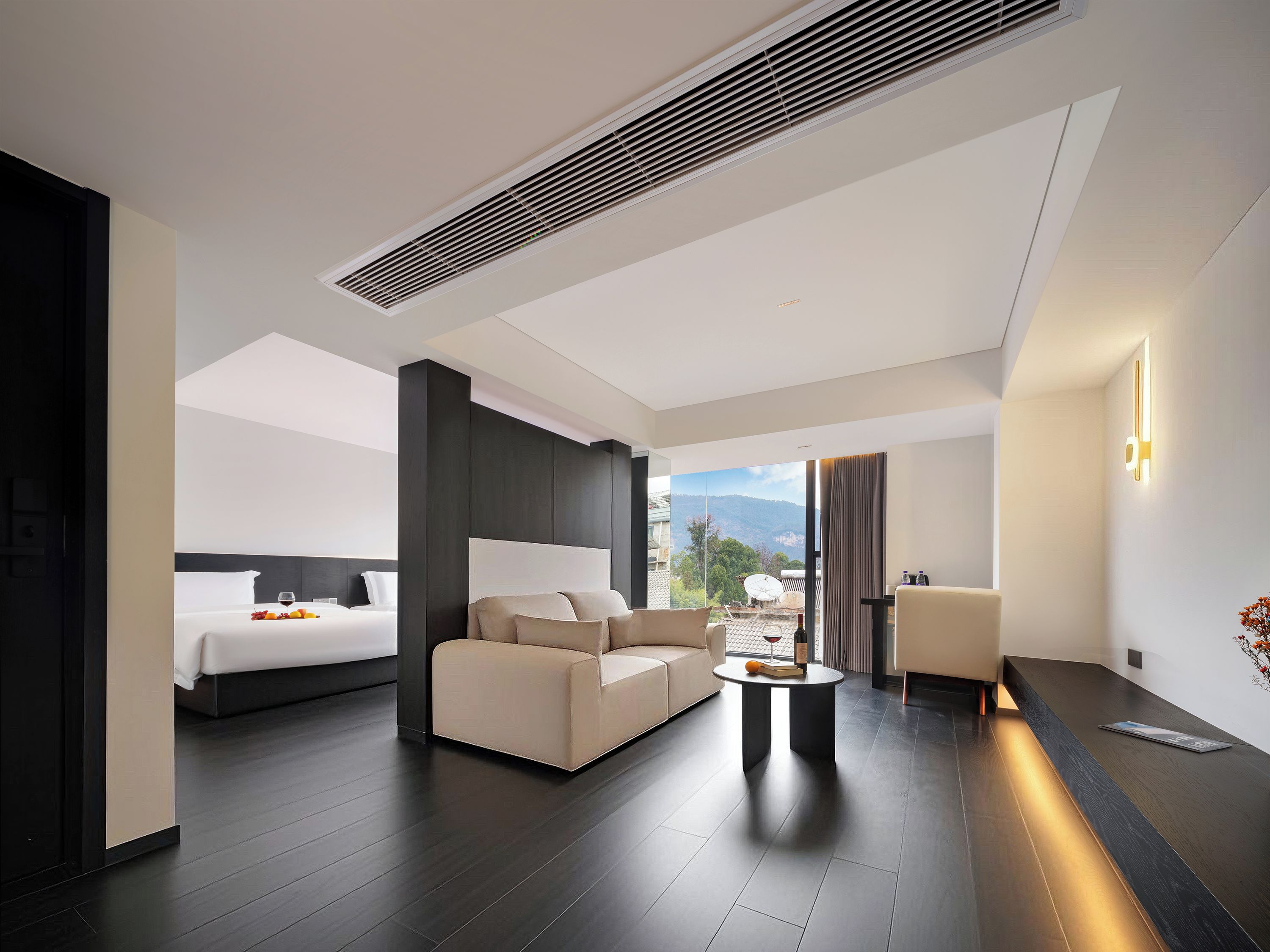 A modern hotel room with a bed, sofa, and a dining area with a table.