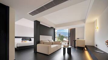 A modern hotel room with a bed, sofa, and a dining area with a table.