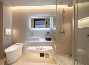 Ein modernes Badezimmer mit einer gläsernen Duschkabine, einer weißen Toilette, einem Marmorwaschbecken und einem Spiegel mit integrierter Beleuchtung.