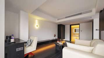 Una camera d'albergo moderna con un divano, un tavolino, un minibar e un punto luce a parete.