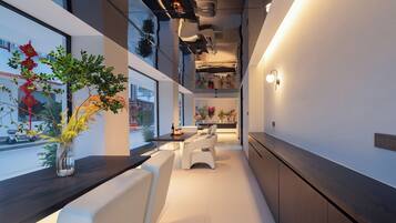 A modern interior with a long dining table, white cushioned seating, and a view through large windows.